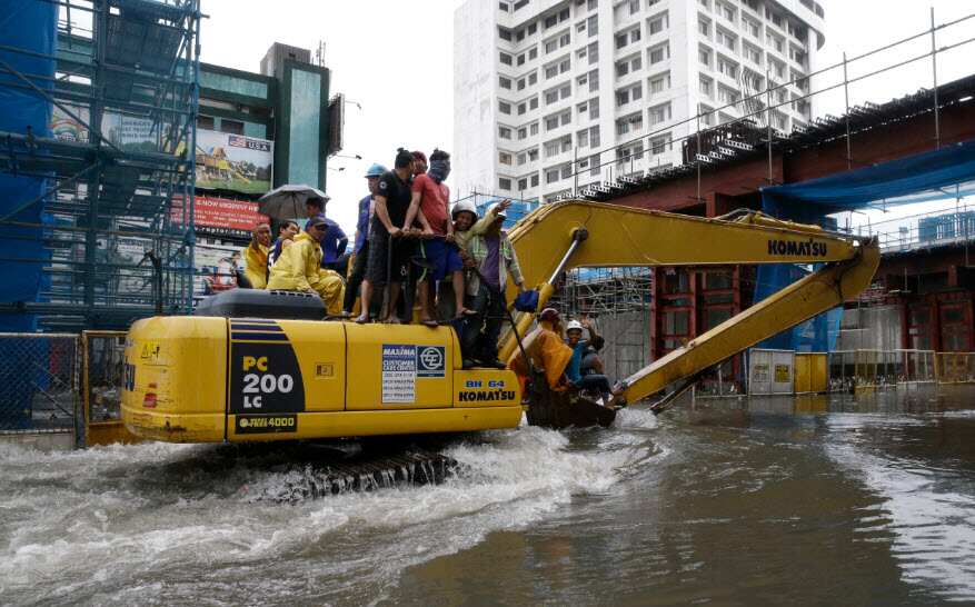 Filipino workers ride on a backhoe as they cross a flooded street in Manila, Philippines 