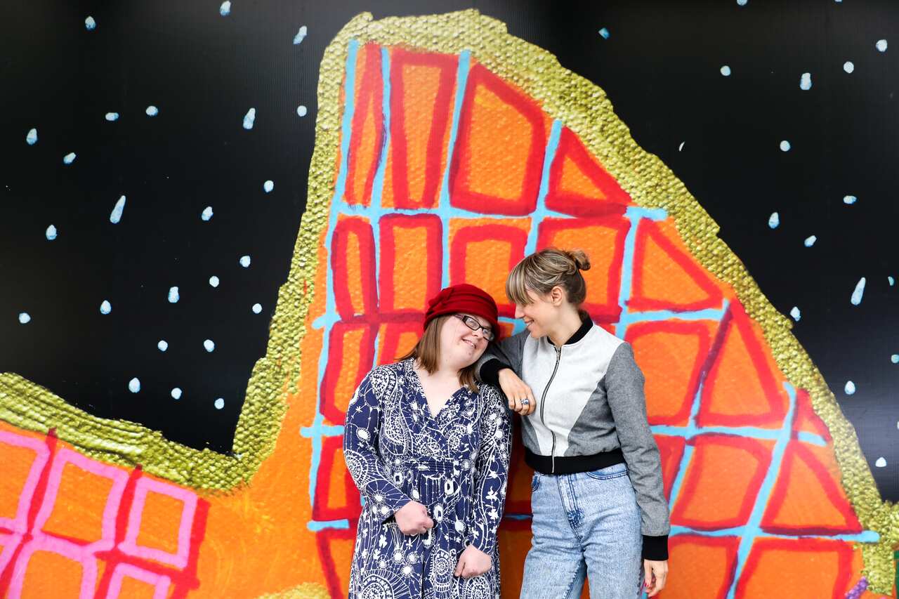 Studio A artist Emily Crockford (left) with artistic director Gabrielle Mordy pose in front of one of Emily’s hoarding designs in Sydney. 