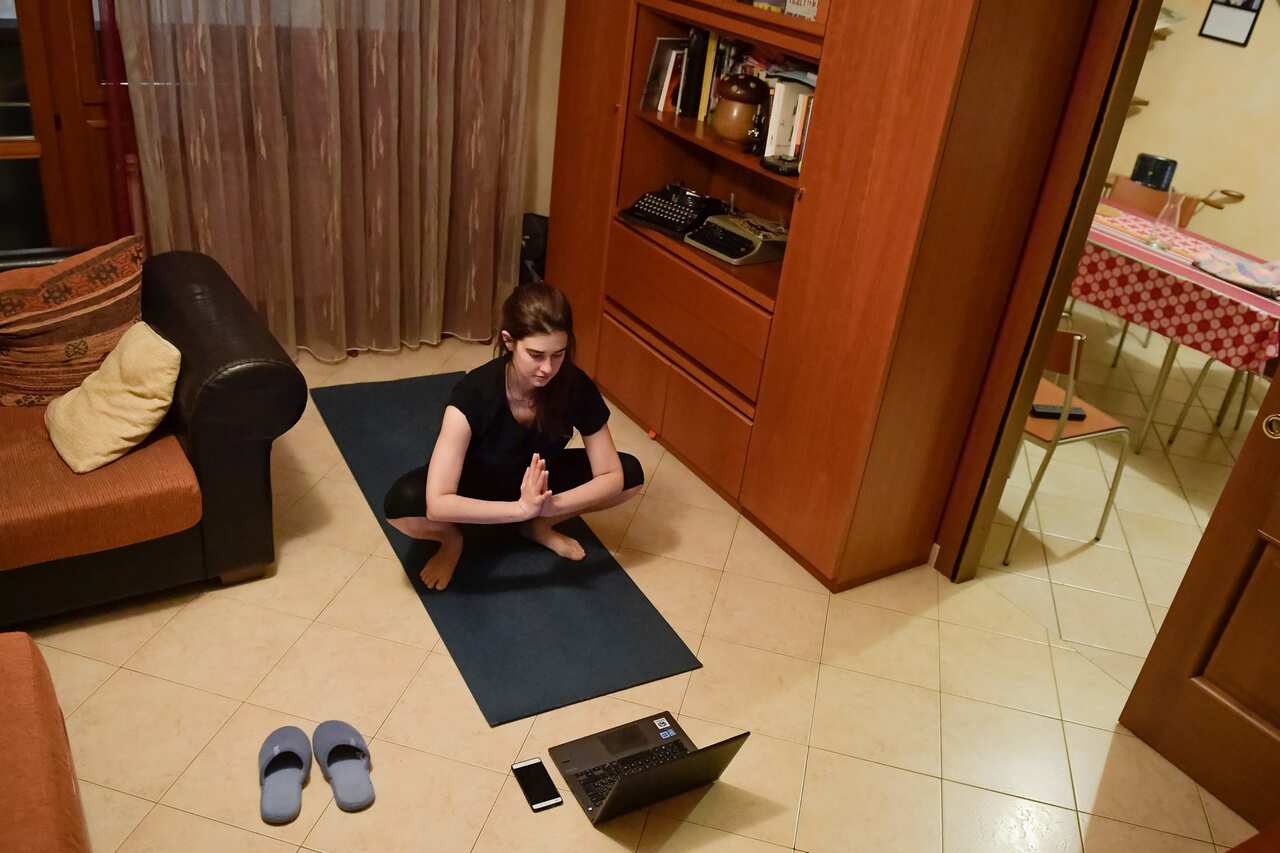 A girl follows an online yoga class from her home