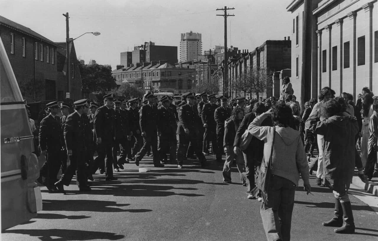 A black and white photo depicting dozens of police officers outside a police station in the 1970s.