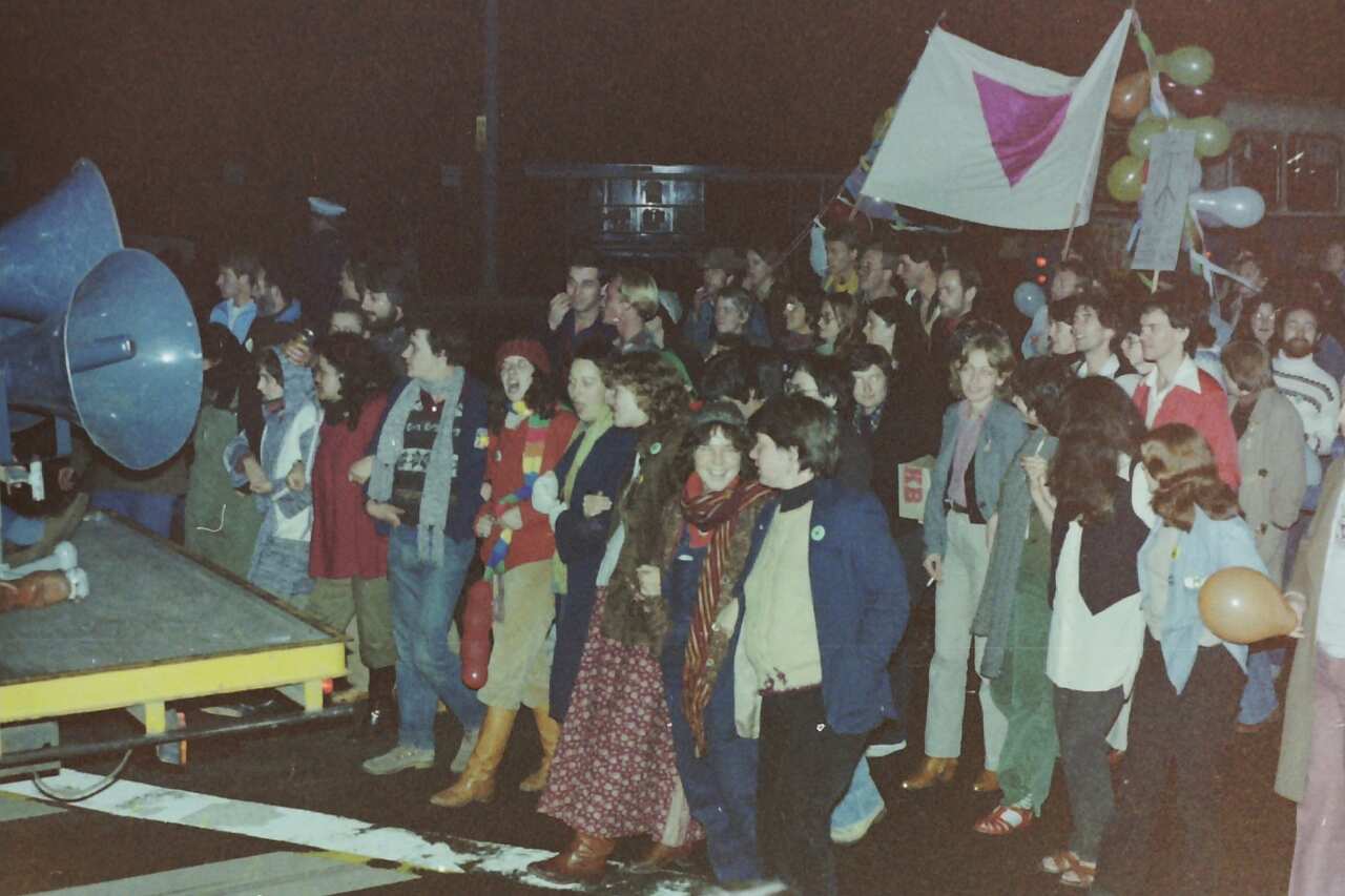 A grainy picture depicting people marching and holding a pink triangle.