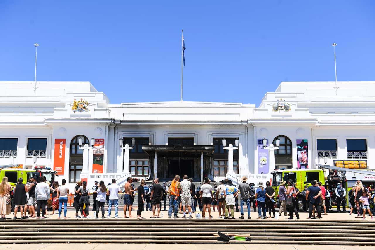 Protesters stand in front of the burned out entrance doors to Old Parliament House in Canberra.