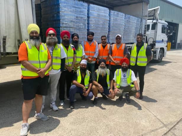 Members of the Sikh community stand in front of a truck filled with water supplies.