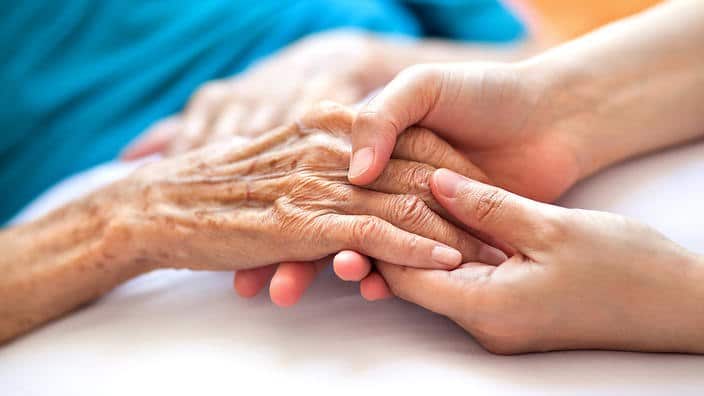 Woman holding senior woman's hand on bed.