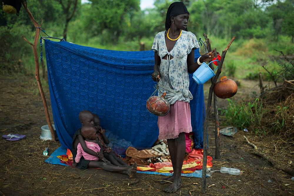 A mother and her children rest under a tarpaulin. Cow's milk, stored in vessels, is their main source of food. (Matthew Abbott)