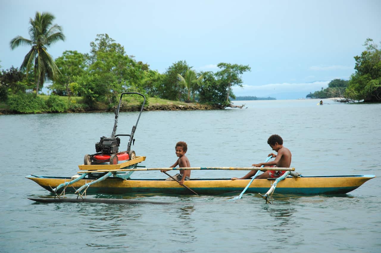 Papua New Guinea: Two boys in an outrigger canoe ferry a lawnmower across a bay near Madang on Papua New Guinea's north coast. 