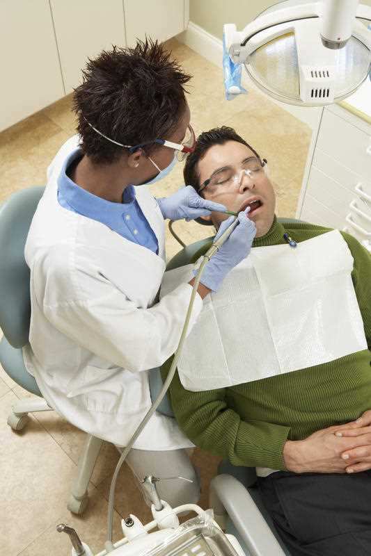A dentist works on the teeth of a man in glasses.