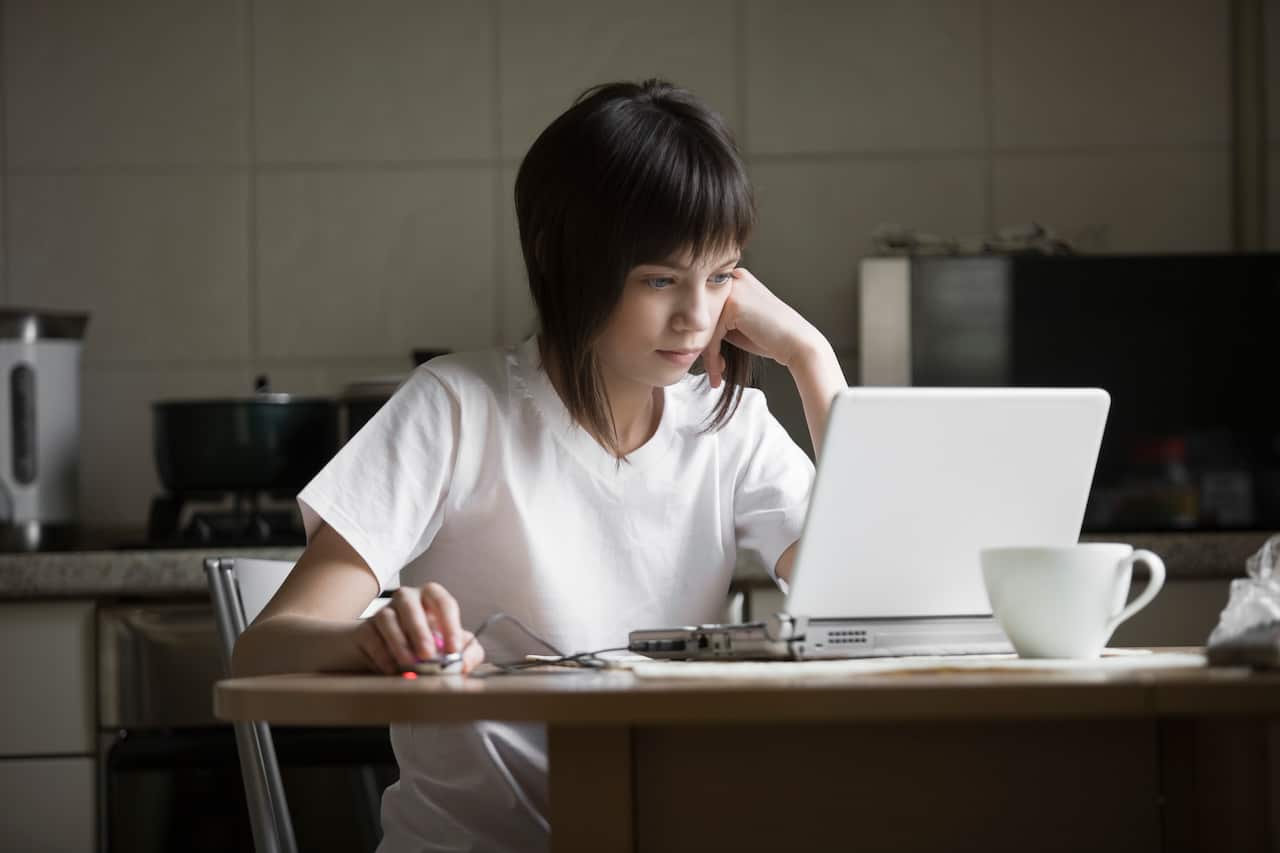 A woman sitting in a kitchen in front of a white laptop
