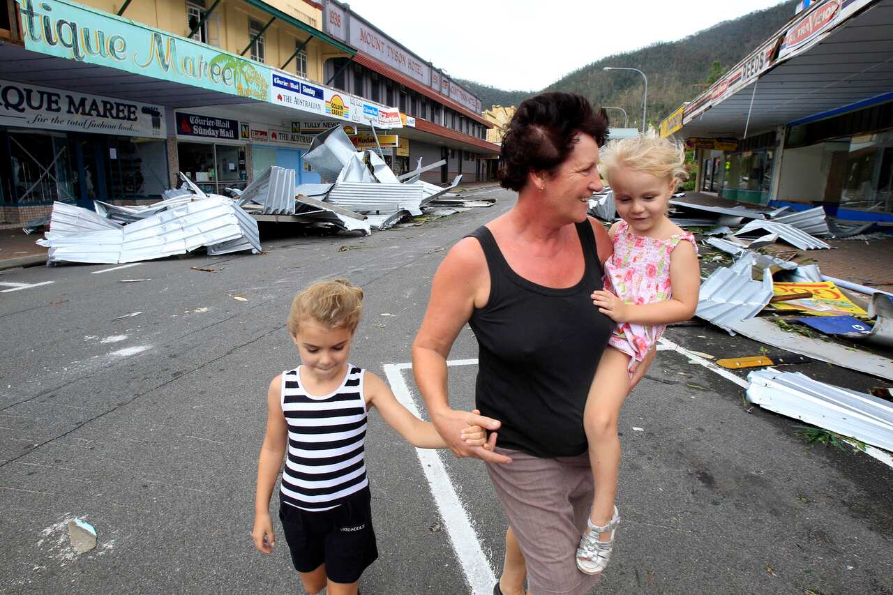Helby Haines walks with her grandchildren Cienna and Claudia past twisted roofing material strewn on the street in Tully, Australia, Feb. 3, 2011.