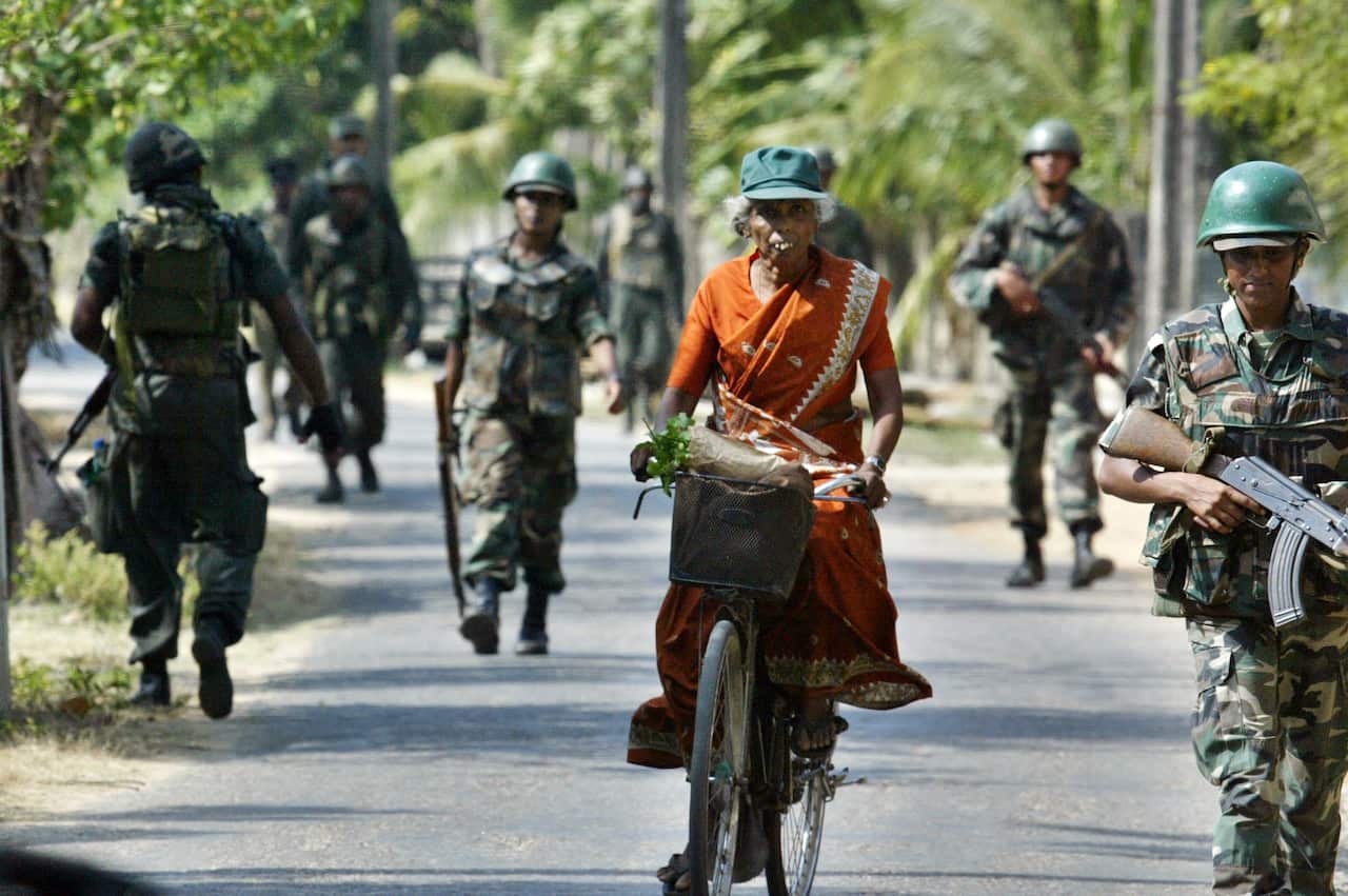 An ethnic Tamil woman rides her bicycle as Sri Lankan army soldiers conduct a cordon and search operation in Jaffna, Sri Lanka, Tuesday, May 16, 2006. 