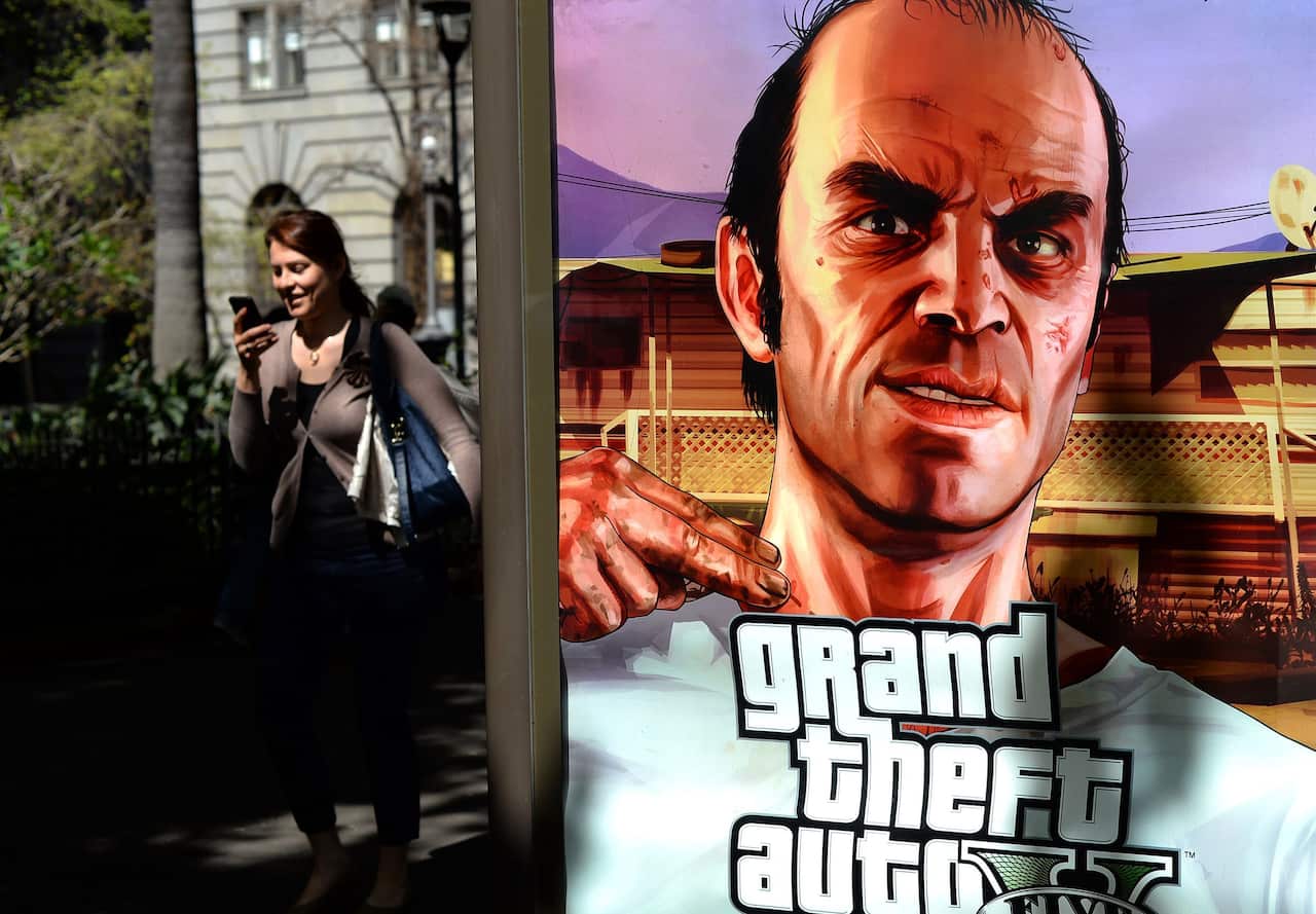 A woman walks past an advertisement for Grand Theft Auto V.