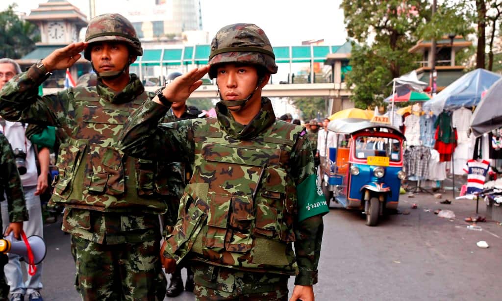 Thai soldiers salute national anthem as they secure the area after grenade attack at anti-government protest site of Ratchaprasong district in Bangkok, Thailand, 23 February 2014. (AAP)