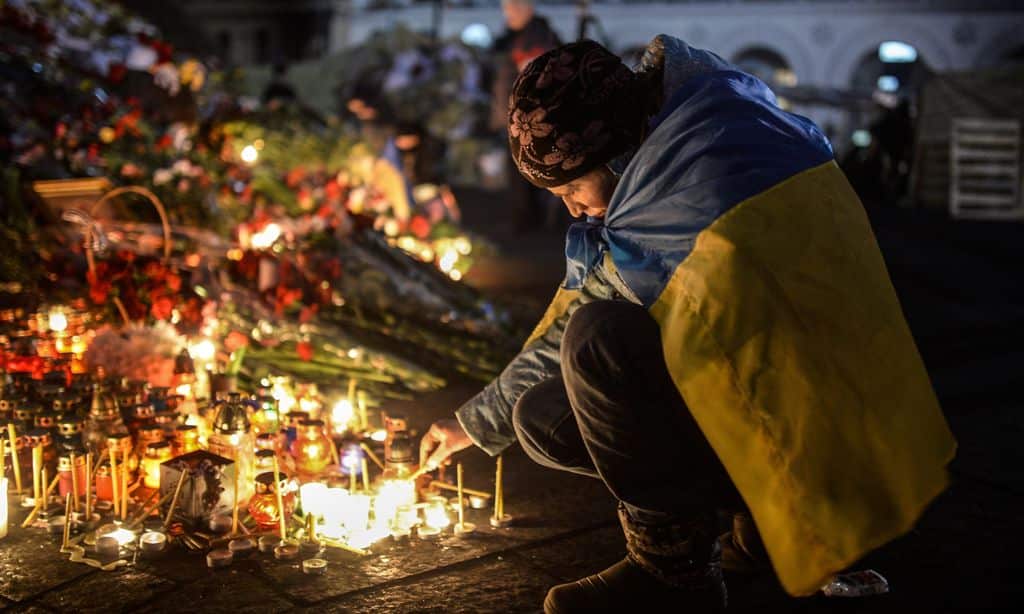 A woman lights a candle at a makeshift memorial to anti-government protesters killed in the past weeks' clashes with riot police on Kiev's Independence Square early on February 24, 2014. (AAP)