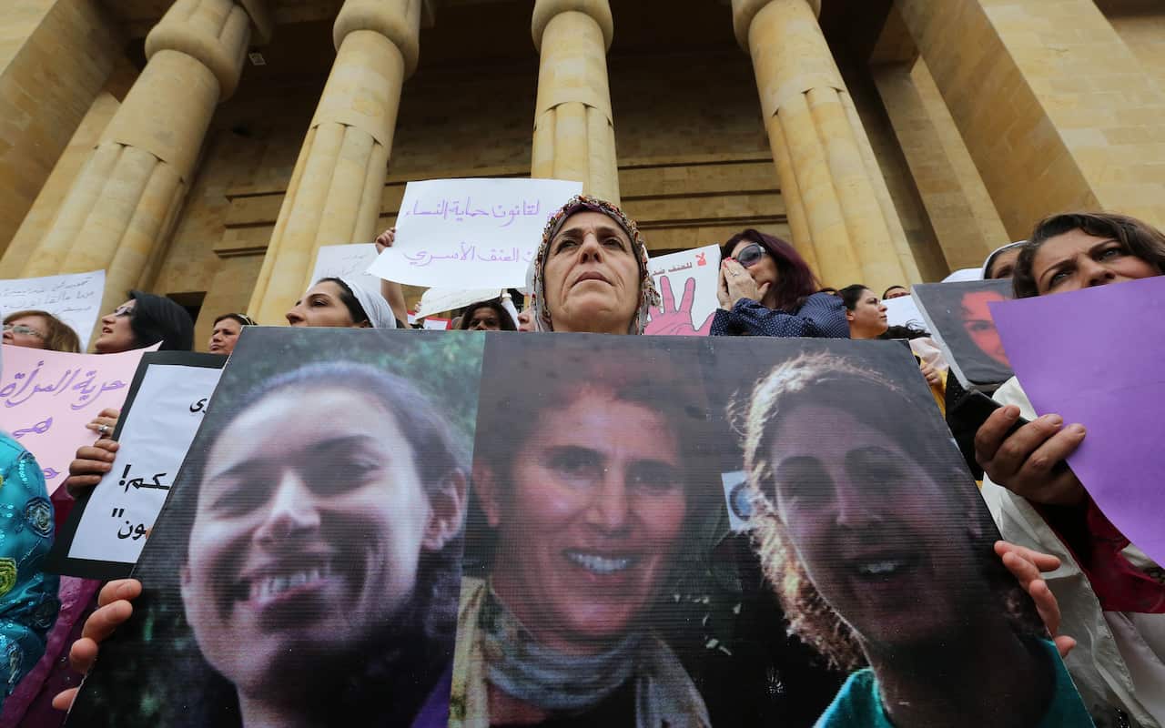 A woman holds portraits of victims of domestic violence during a rally on the "International Women's Day" on March 8, 2014 in front of the National Museum in the capital Beirut. (AAP)