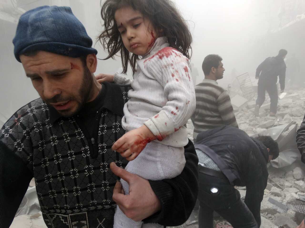 A Syrian man evacuates a child found in the rubble of a building reportedly hit by an explosives-filled barrel dropped by a government forces helicopter on March 18, 2014 in Aleppo. (AAP)