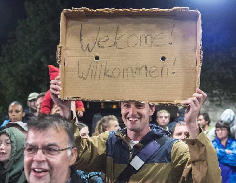 A man holds a cardboard "Welcome" sign during the arrival of refugees at a train station in Germany. (AAP)