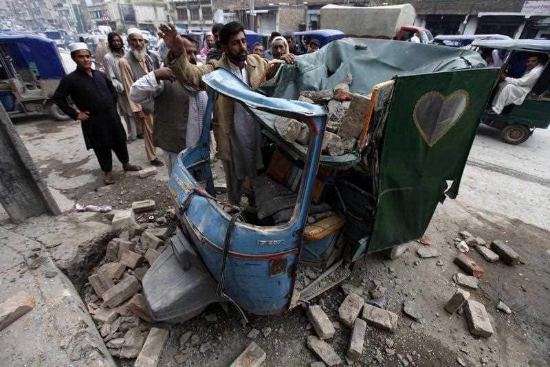 People remove debris from a rickshaw on a road following a 7.5 magnitude earthquake, in Peshawar, Pakistan.