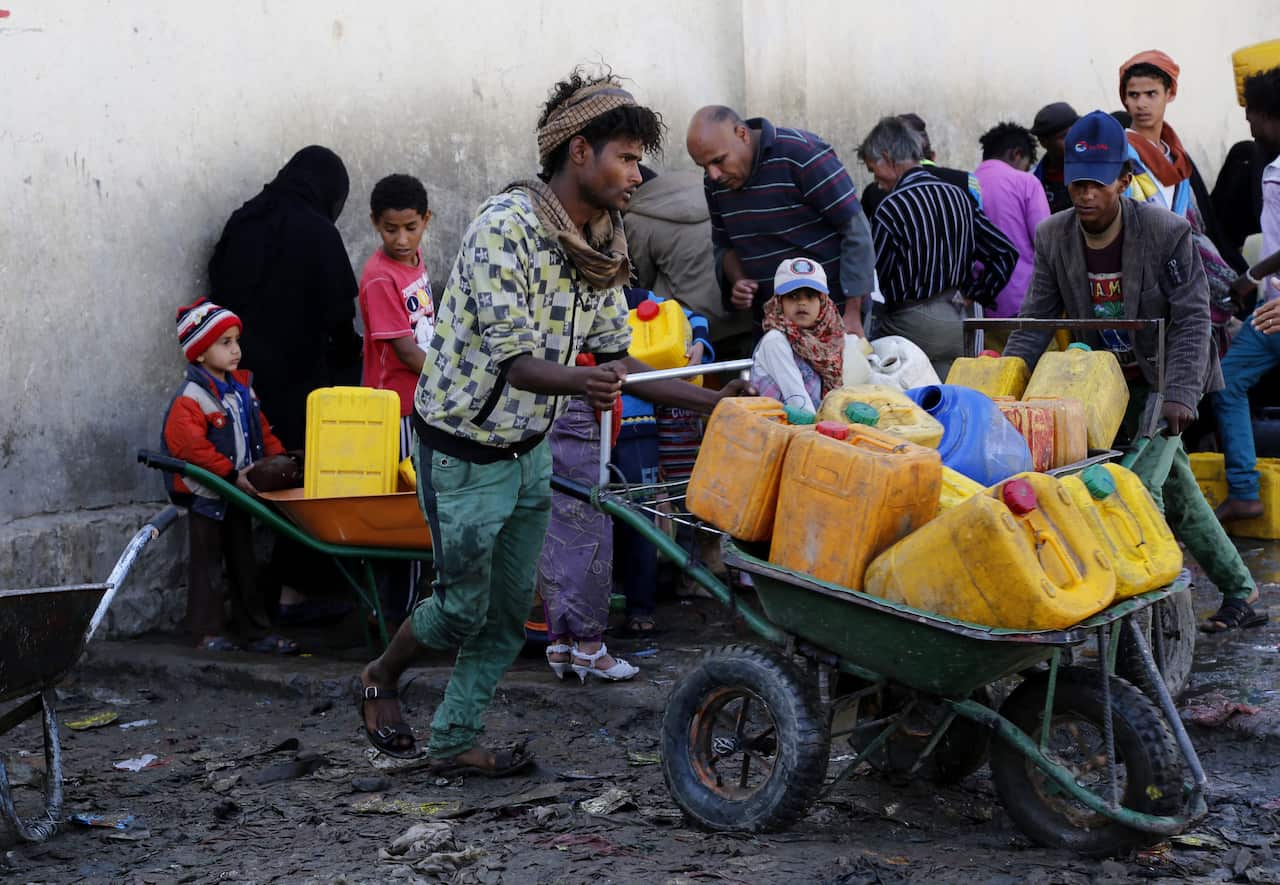 Yemenis push wheelbarrows with jerrycans full of clean water