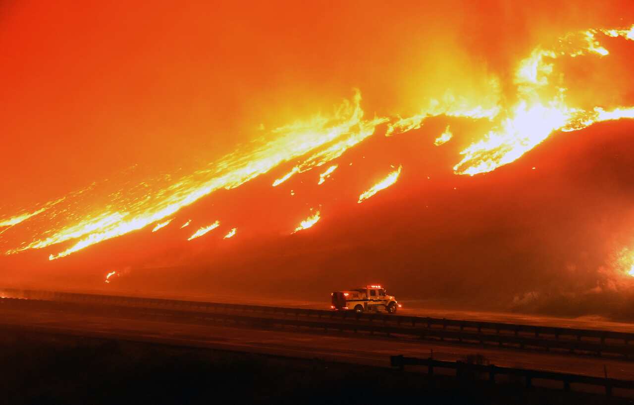 In this photo provided by Ryan Cullom, a Ventura County Fire Department engine holds its positions as fire overruns state Highway 101 near Ventura, Calif., Saturday, Dec. 26, 2015. (Ryan Cullom via AP)