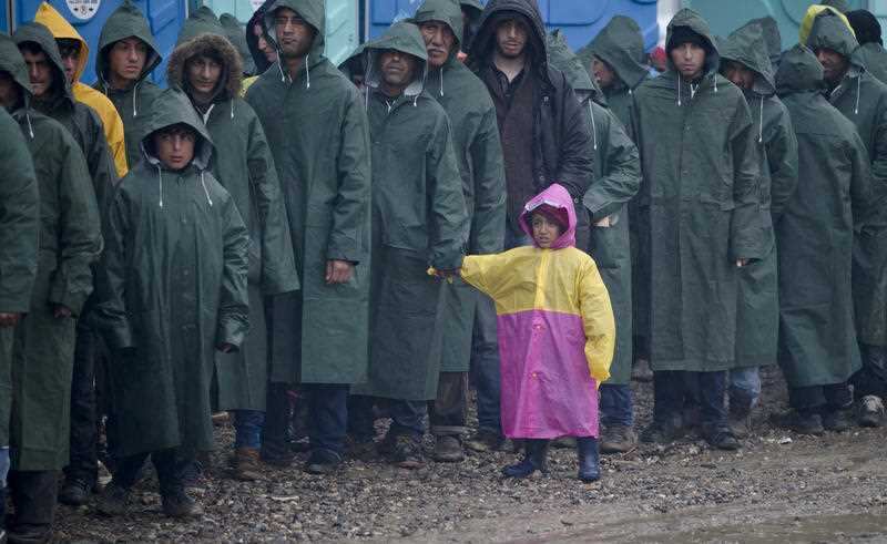 A child waits along with adults for hot soup rations, during heavy rain at the northern Greek border station of Idomeni, Wednesday, March 9, 2016. 