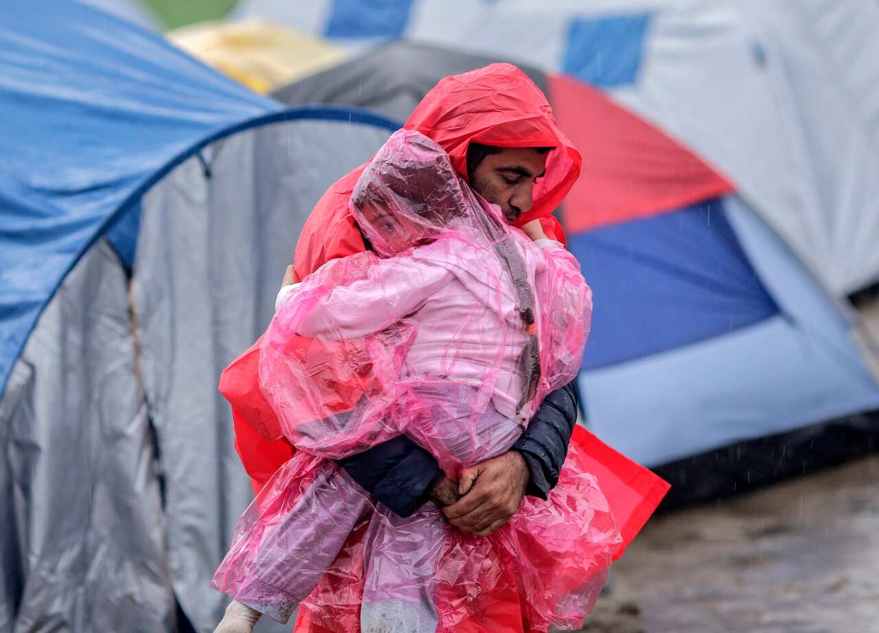 A refugee carries his son in a refugee camp at the border between Greece and the Former Yugoslav Republic of Macedonia