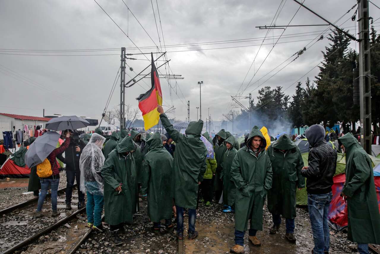 Refugees protest waving a German flag in a refugee camp at the border between Greece and the Former Yugoslav Republic of Macedonia 