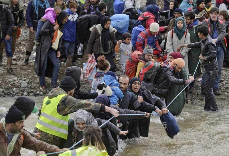 Migrants cross a river, north of Idomeni, Greece, attempting to reach Macedonia on a route that would bypass the border fence, Monday, March 14, 2016.