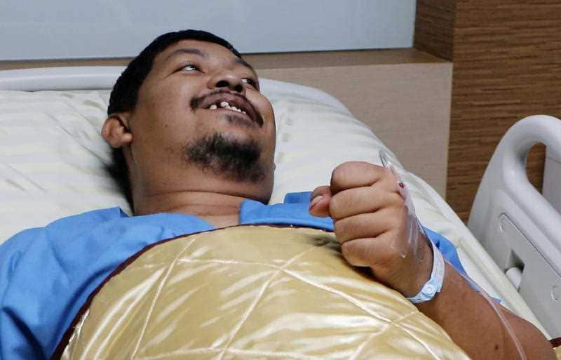 Attaporn Boonmakchuay gestures while talking to reporters, while lying in a hospital bed following a snake attack at his home in Chachoengsao
