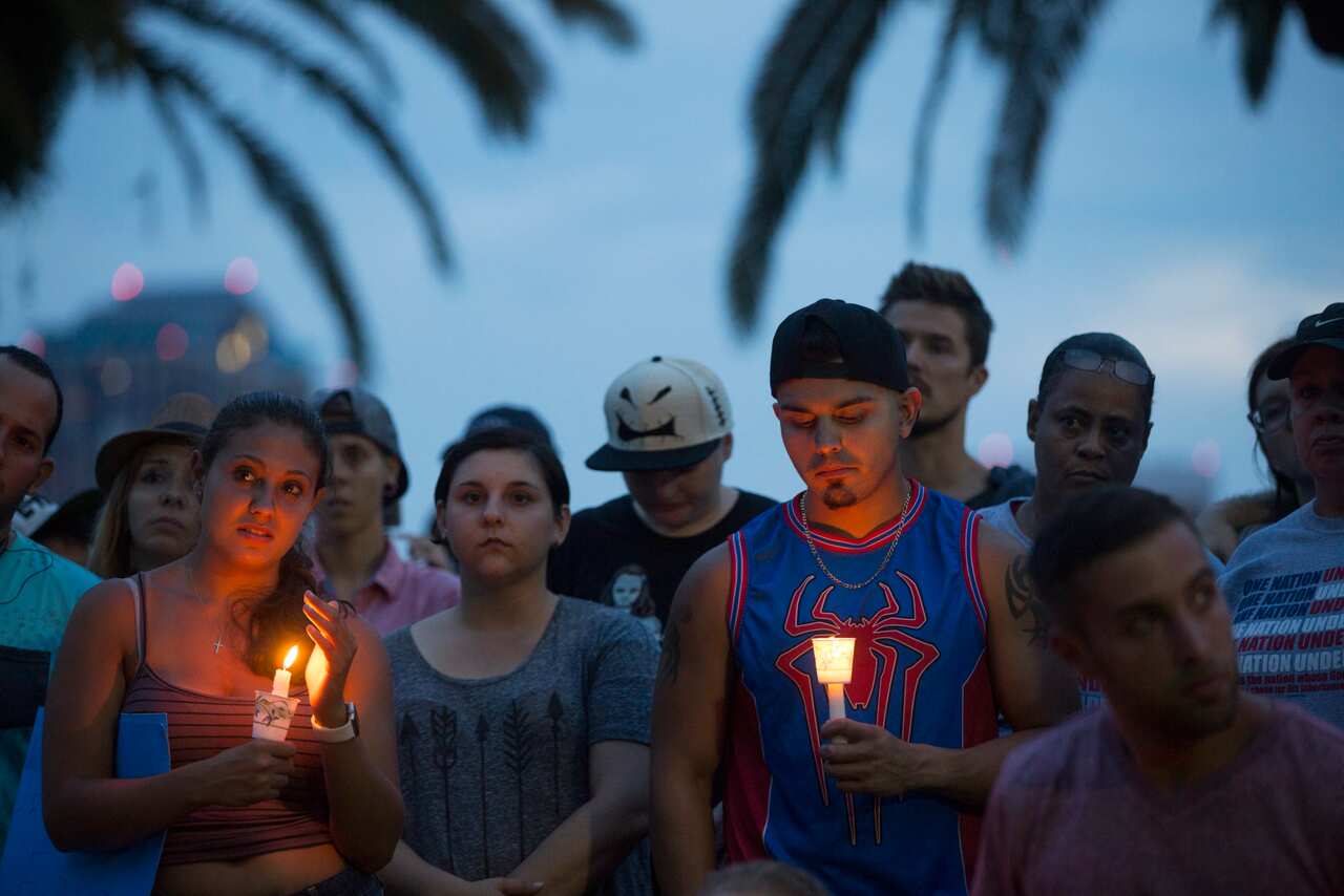 A row of people mourne holding candles in the twilight.