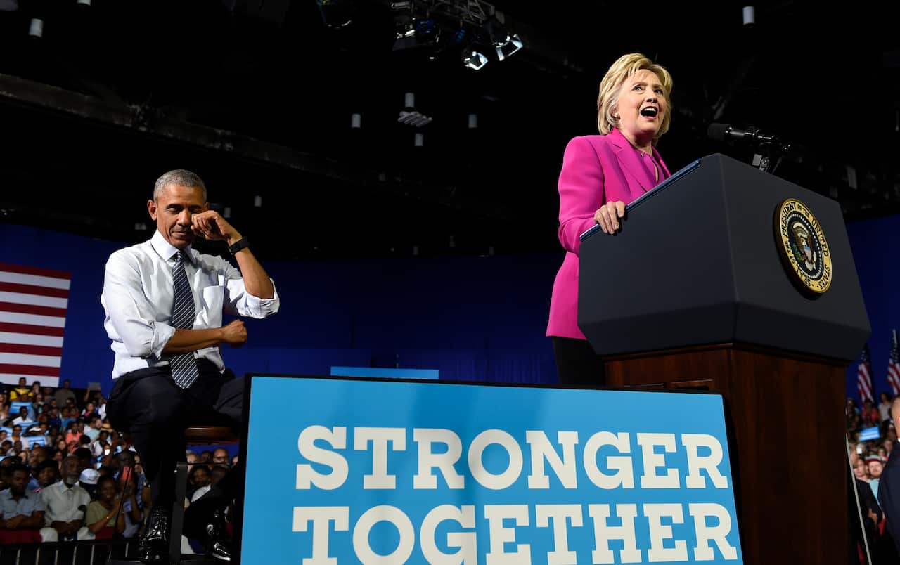 Obama and clinton at a campaign rally. A sign reads 'stronger together'