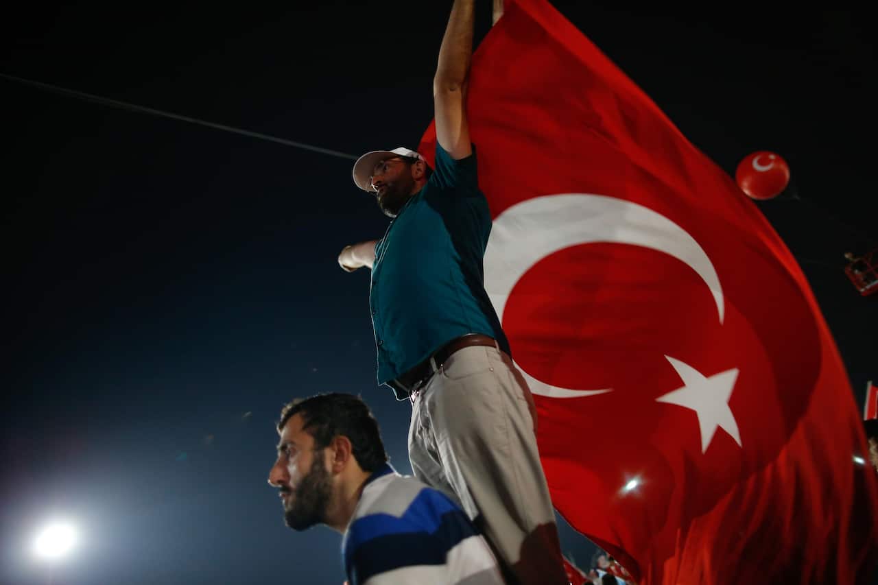 A Turkish man holds up the flag of his country during the speech of President Recep Tayyip Erdogan in Istanbul, Sunday, Aug. 7, 2016. 