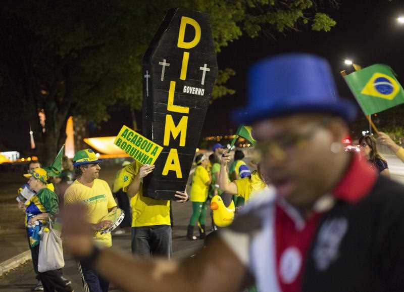 A pro-impeachment demonstrator holds a sign that reads in Portuguese "The end of the little mouth" and a cardboard coffin