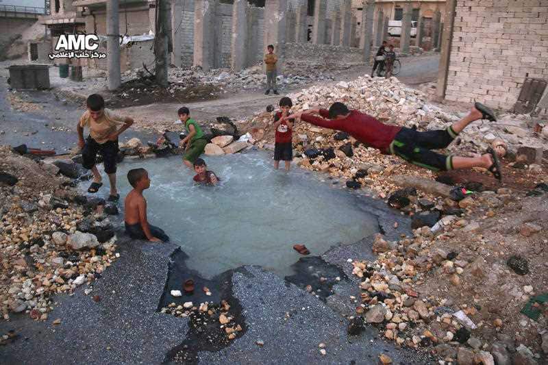 Syrian boys dive into a hole filled with water that was caused by a missile attack in the rebel-held neighborhood of Sheikh Saeed in Aleppo