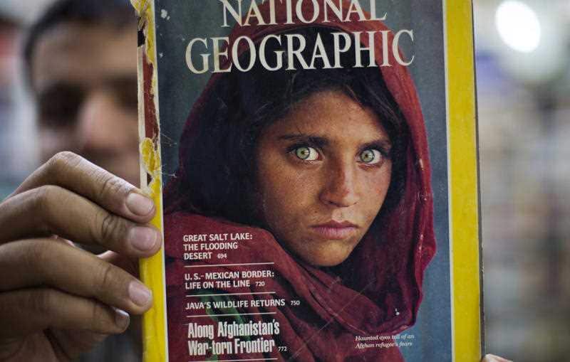 Pakistan's Inam Khan, owner of a book shop shows a copy of a magazine with the photograph of Afghan refugee woman Sharbat Gulla, from his rare collection in Islamabad, Pakistan, Wednesday, Oct. 26, 2016.