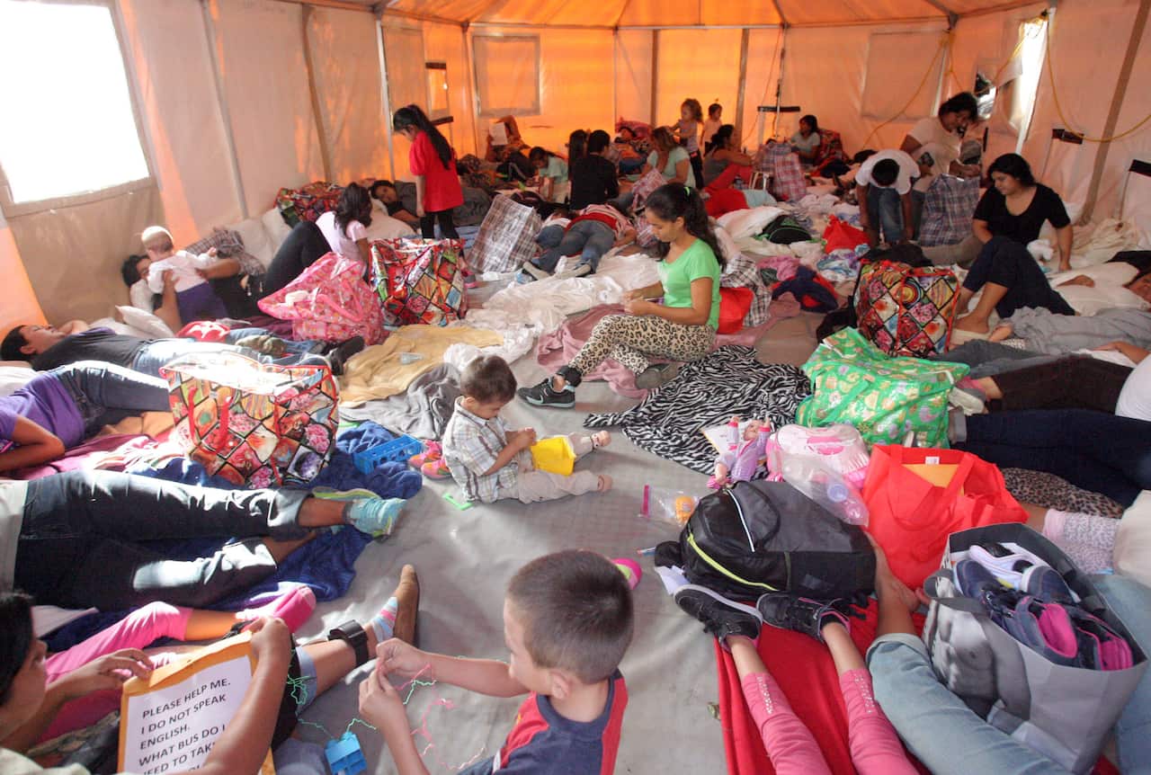 Central American mothers and their children take a place on the floor of a portable tent at the Humanitarian Respite Center in Texas.  