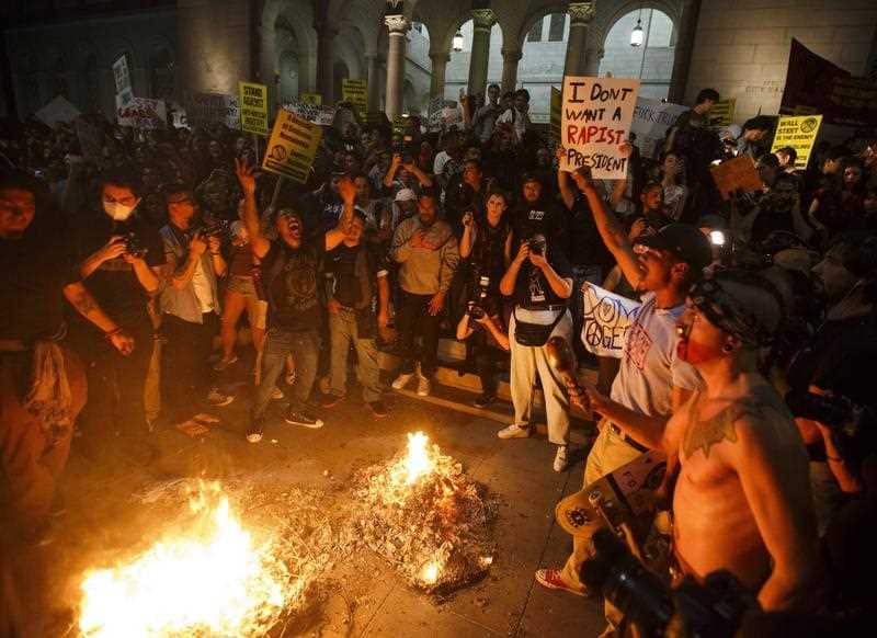 Demonstrators chant in front of a fire they lit in protest against President-elect Donald Trump outside the City Hall building in Los Angeles, California, USA