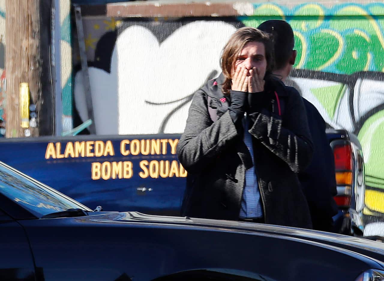 A person reacts as coroners begin work and firefighters and investigators continue work at the scene of a deadly warehouse fire in Oakland.