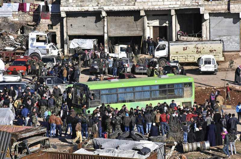 Residents gather near a green government bus for evacuating from eastern Aleppo, Syria, Thursday, Dec. 15, 2016