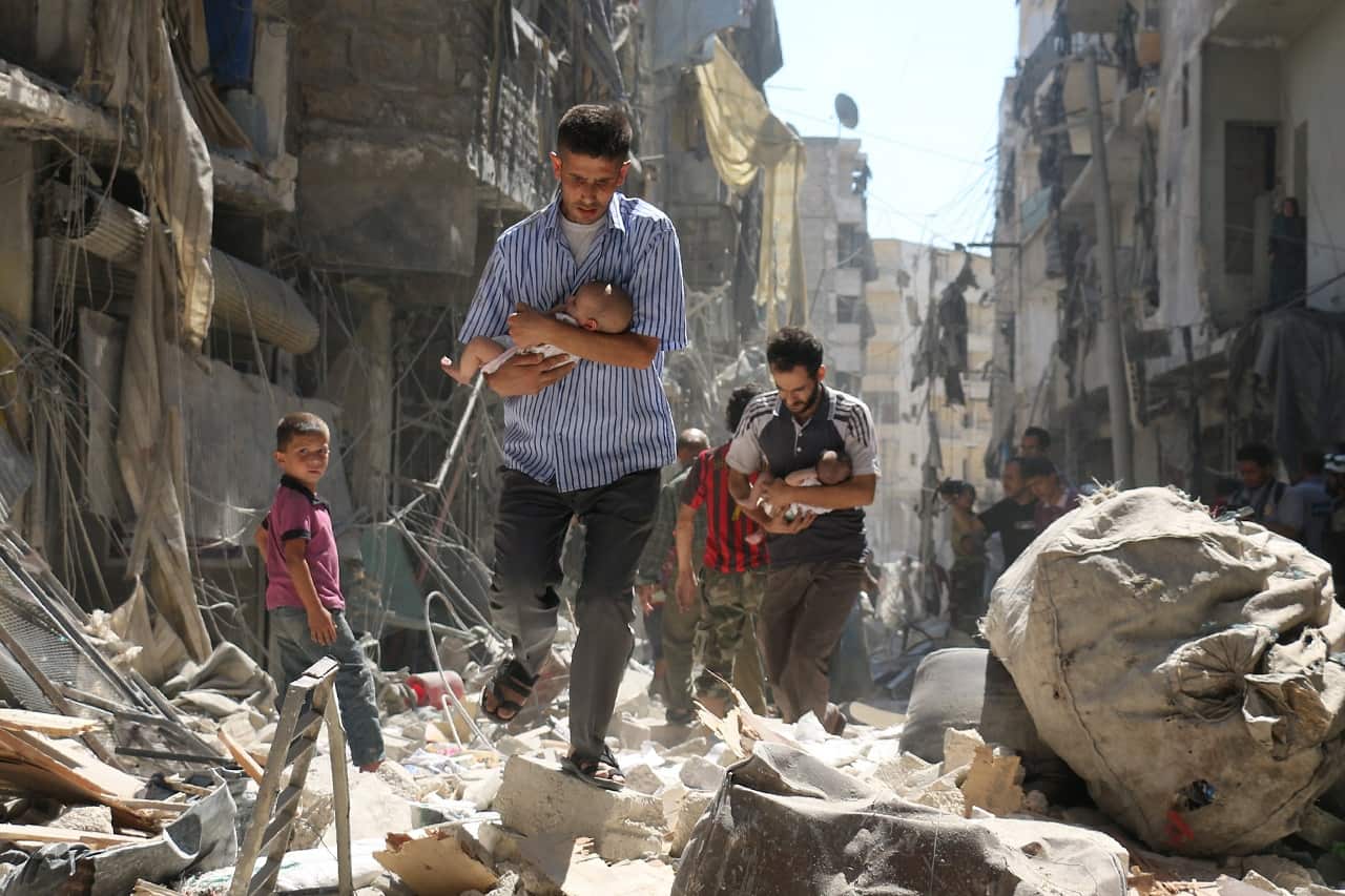 Men carry babies through rubble in Aleppo in 2016.