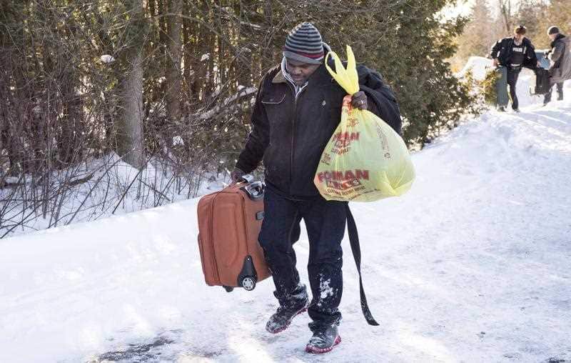 A Somali man carries his belongings after crossing into Canada over the U.S.-Canada border near Hemmingford, Quebec