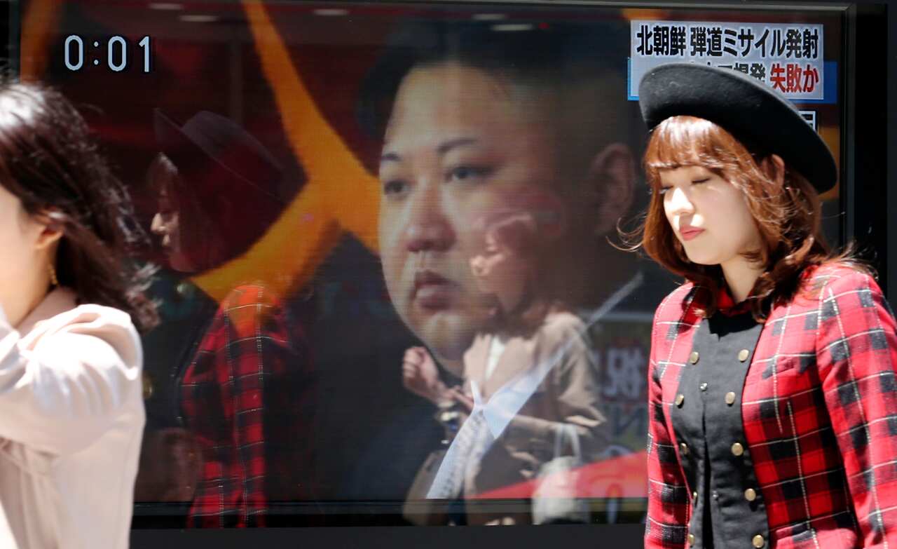 People in Tokyo walk past a TV news report showing an image of Kim Jong Un while reporting North Korea's rocket launch.