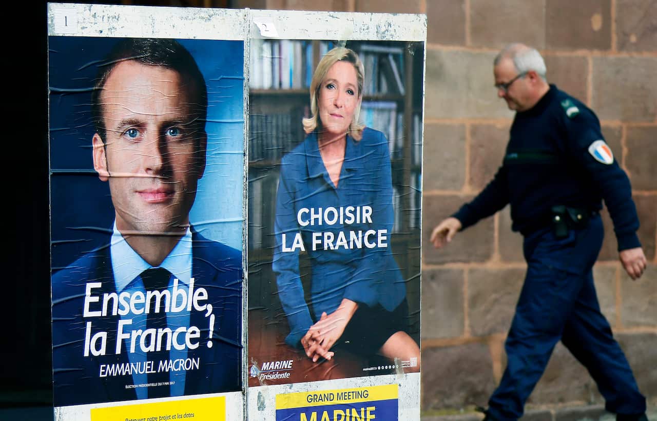 A police officer walks near election campaign posters for Emmanuel Macron and Marine Le Pen.