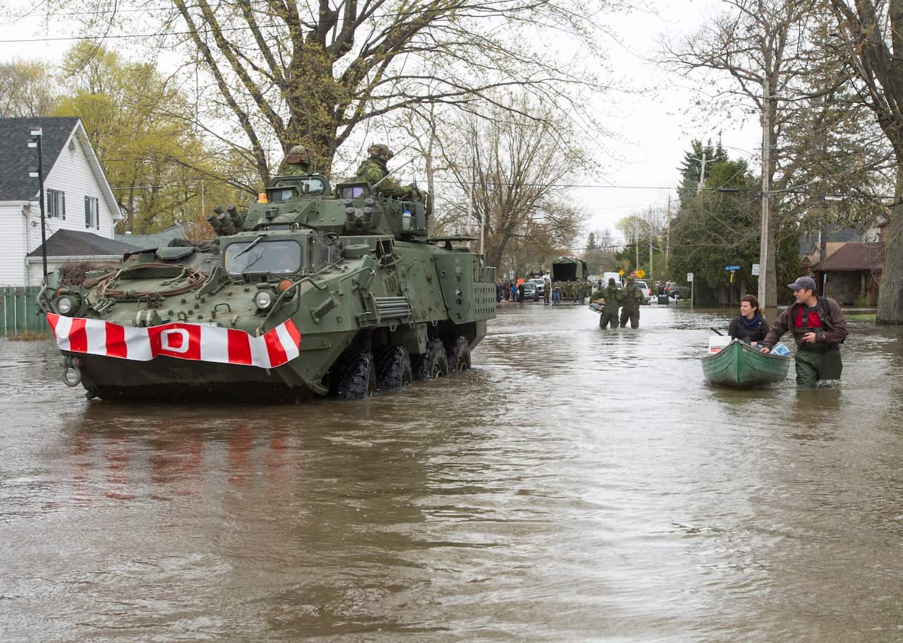 A Canadian Forces LAV, light armoured vehicle, passes a couple in their canoe on the flooded streets, Monday, May 8, 2017 in Deux-Montagnes, Que. (Ryan Remiorz/The Canadian Press via AP)