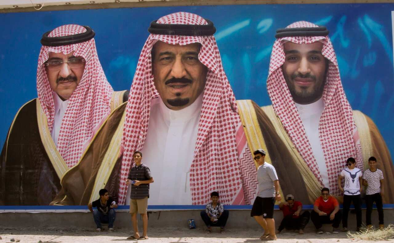 Saudi boys pose in front of a huge billboard showing King Salman, with his 31-year-old son Mohammed bin Salman and Prince Mohammed bin Nayef.