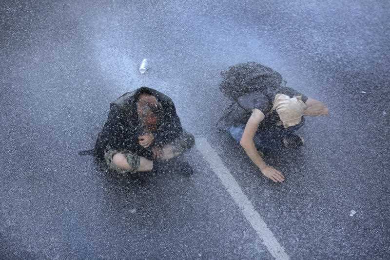 Two protesters sit on a street while the Police uses a water canon during a protest against the G-20 summit in Hamburg, northern Germany,