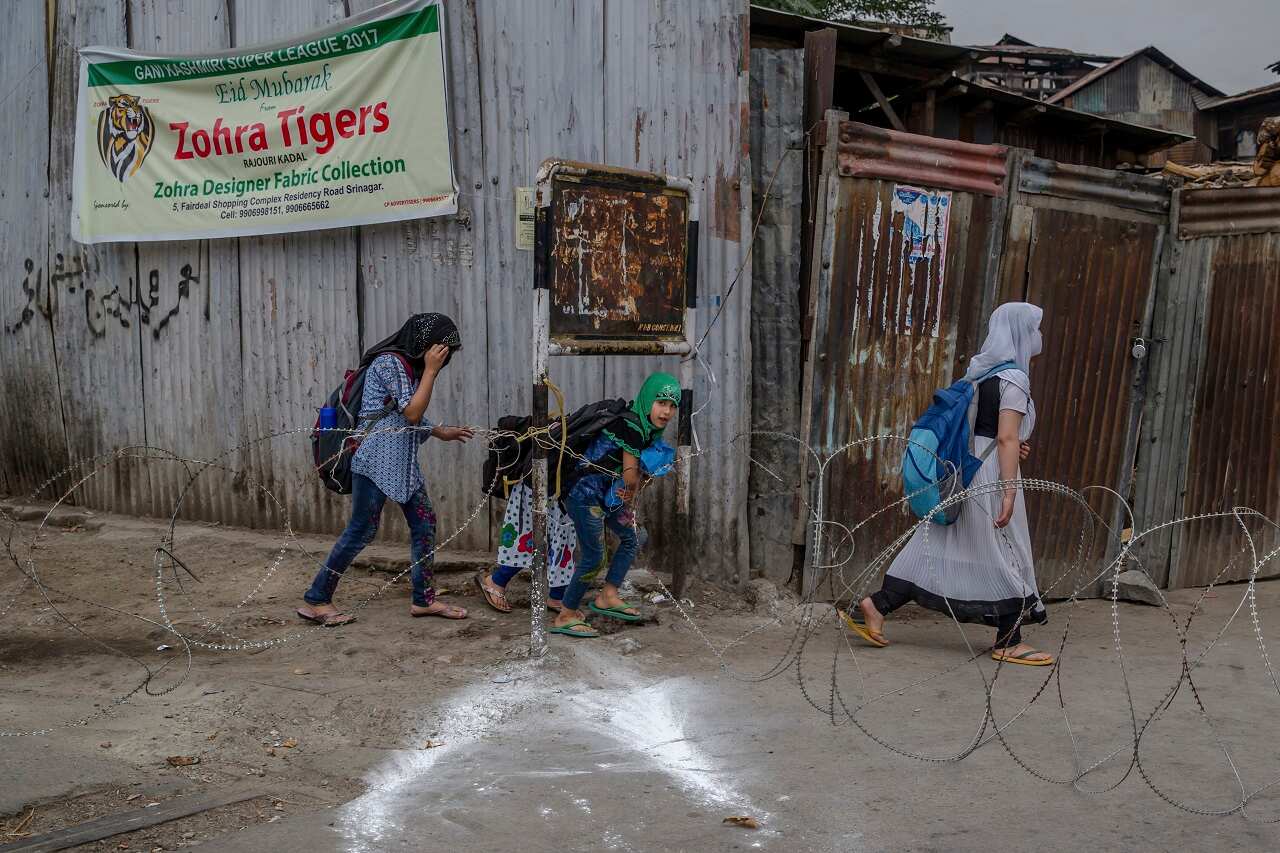 Kashmiri girls walk past a barbed-wire road checkpoint in Srinagar, Indian controlled Kashmir.