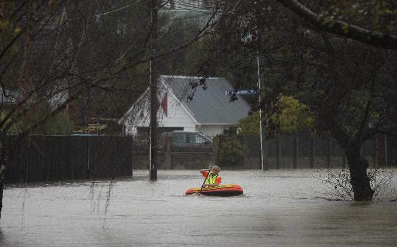 A resident paddles a inflatable canoe in his flooded street in Christchurch