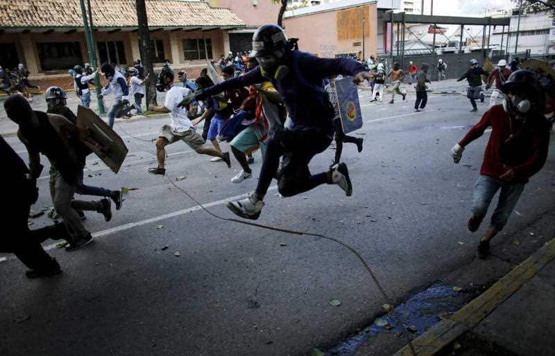 Anti-government protesters run from advancing Venezuelan Bolivarian National Guard officers on the first day of a 48-hour general strike