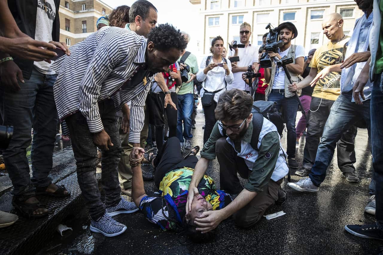 A woman lies on the ground after being struck by the water of water cannons used by Italian law enforcement officers