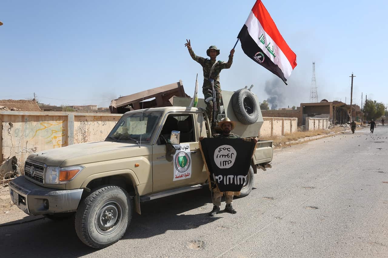 Fighters of Hashed Al-Shaabi wave an Iraqi flag and hold another one bearing the logo of lS as Iraqi forces advance inside the town of Tal Afar, west of Mosul.